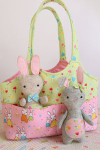 pink and green bag with outside pockets.There is a fet rabbit standing in front and another one in the pocket