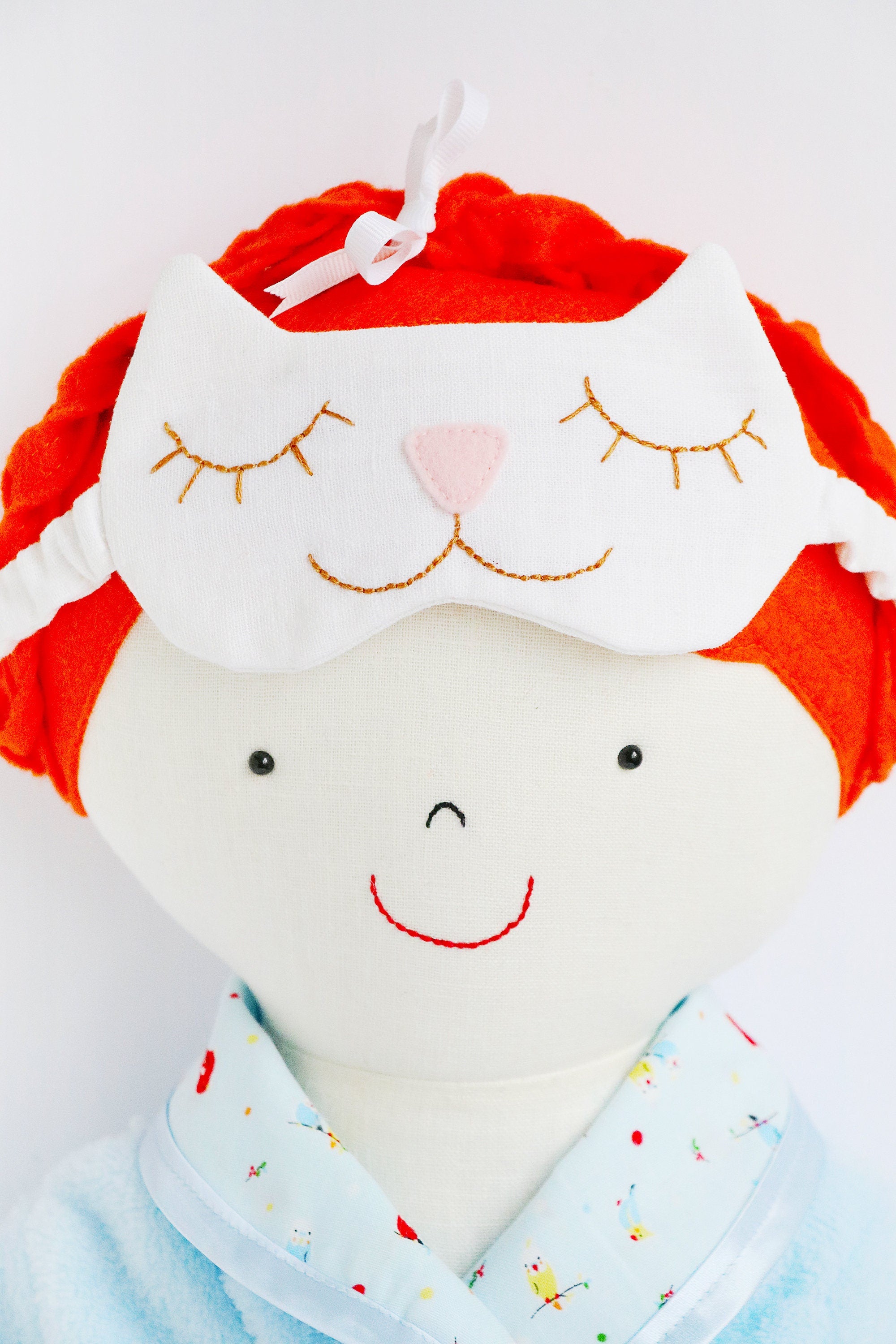 close up of cloth doll face with kitty sleep mask resting on her head.