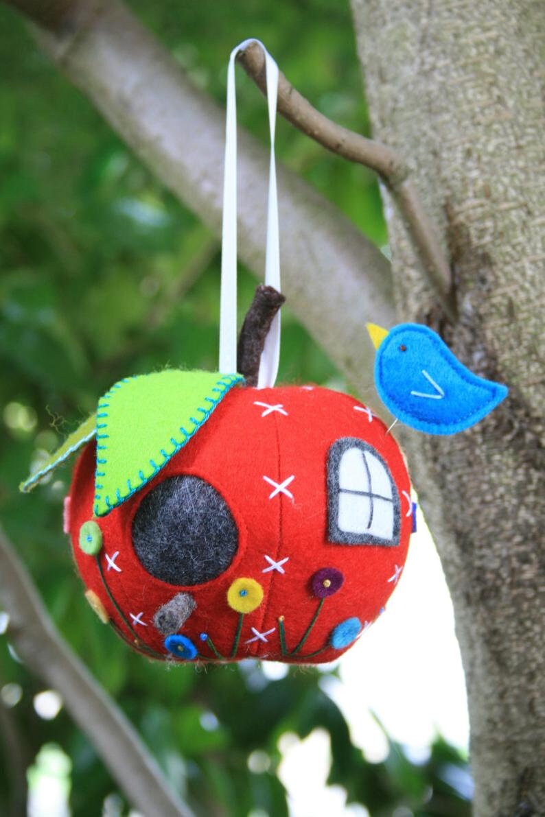 red felt apple shaped pincushion decorated like a house with embroidered flowers and a bluebird pin