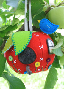 red felt apple shaped pincushion decorated like a house with embroidered flowers and a bluebird pin